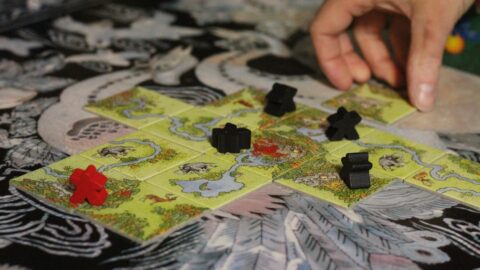 Carcassonne tile placement game board with meeples claiming features