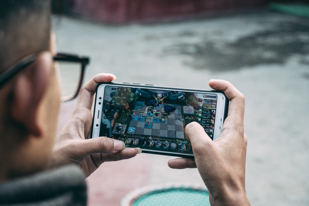 A physical board game box sits on a table next to a smartphone displaying a digital code, highlighting the contrast between tangible and digital rewards.