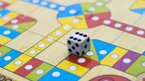 A close-up of a wooden worker placement game board with three distinct player figures placed on limited action spaces, highlighting the concept of spatial denial.